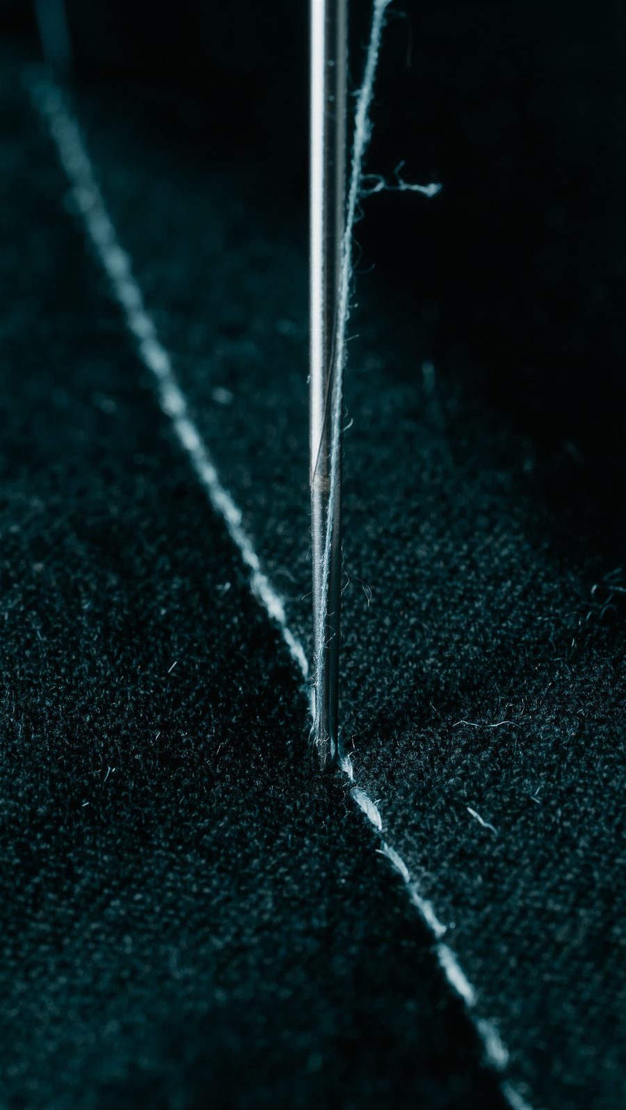 Macro of a needle and stitched thread on black fabric